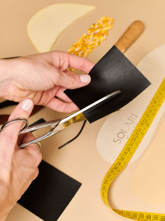 Hands cutting black fabric with scissors in a workspace highlighting ethical fashion practices.