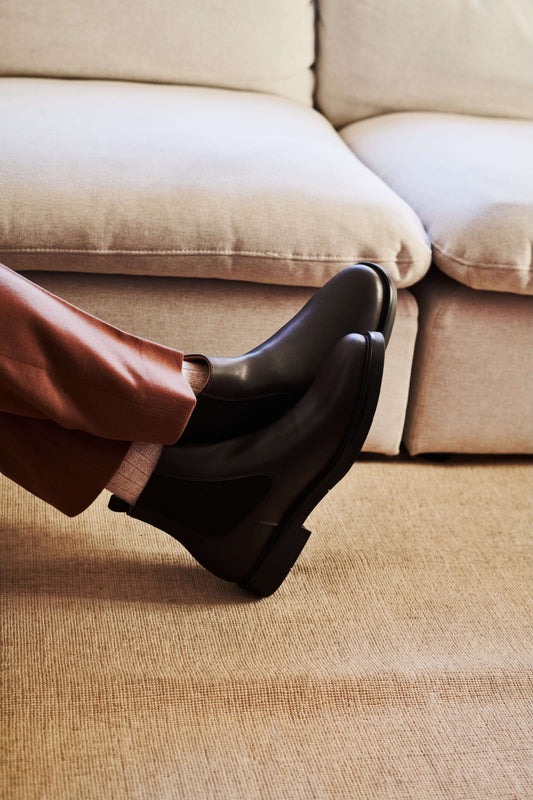 A stylish pair of High-Quality Vegan Chelsea Boot worn with brown trousers on a couch.